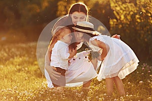 Happy family of mother, little son and daughter spending free time on the meadow at sunny day time of summer