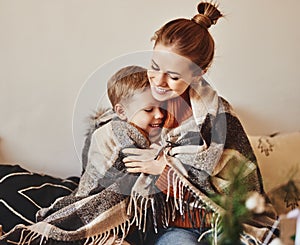 Happy family mother and loving son hug and laugh wrapped in a warm blanket on a cozy winter evening