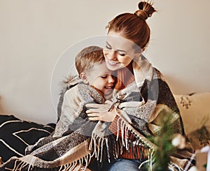 Happy family mother and loving son hug and laugh wrapped in a warm blanket on a cozy winter evening photo