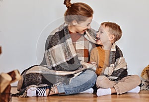Happy family mother and loving son hug and laugh wrapped in a warm blanket on  evening at home
