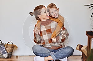 Happy family mother and loving son in warm sweaters hug and laugh sitting on floor near wall  at home