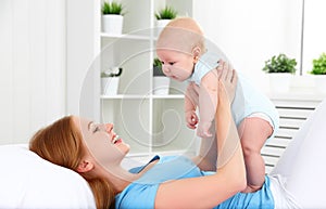 Happy family mother playing with baby in bed