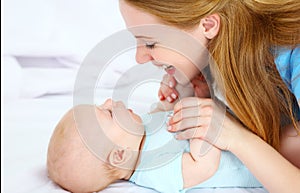 Happy family mother playing with baby in bed