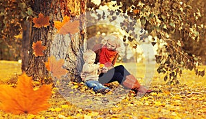 Happy family mother playing with child son in autumn park with yellow leaves