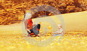 Happy family mother playing with child son in autumn park with yellow leaves