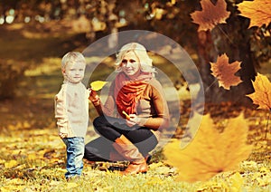 Happy family mother playing with child son in autumn park with yellow leaves