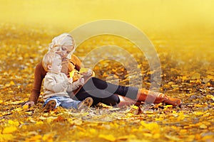 Happy family mother playing with child son in autumn park with yellow leaves