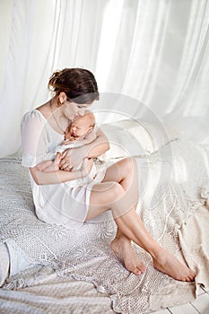 Happy family mother playing and hug with newborn baby in bed