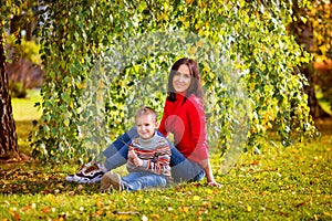 Happy family mother and son boy with sweet emotions hug in autumn in nature, seeing on the grass near a tree