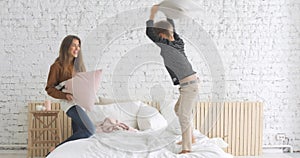 Happy family mother and son having funny pillow fight on bed in nursery at home.