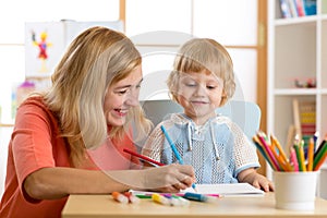 Happy family - mother and son toddler together paint. Adult woman helps to child boy.