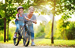 Happy family mother teaches child daughter to ride a bike in the Park