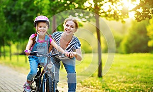 Happy family mother teaches child daughter to ride a bike in the Park