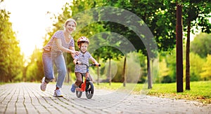 Happy family mother teaches child son to ride a bike in the Park