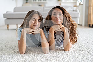 Happy family mother and teenage girl daughter lying on carpet in living room and smiling at camera