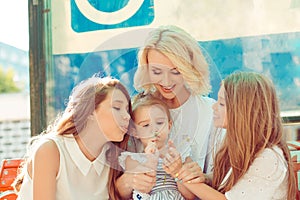 Happy family mother and three girls blowing on a dandelion flower