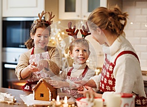 Happy family mother and two kids in xmas aprons decorating Christmas honey gingerbread house