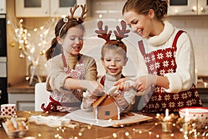 Happy family mother and two kids in xmas aprons decorating Christmas honey gingerbread house