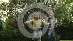 Happy family mother, two Three little siblings kids are blowing soap bubbles and enjoying summer holidays in garden or
