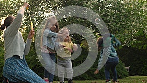Happy family mother, two Three little siblings kids are blowing soap bubbles and enjoying summer holidays in garden or