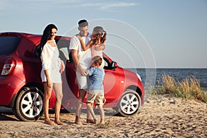 Happy family near car on sandy beach, space for text. Summer trip