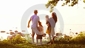 Happy family near the sea. Field and trees in countryside. Warm colors of sunset or sunrise. Loving parents and