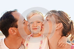 Happy family near to sea, parents kiss daughter