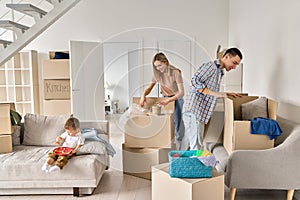 Happy family new home owners with child unpacking cardboard boxes on moving day.