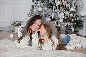 Happy family on New Year Eve. Young beautiful mother and little cute daughter in white cozy sweaters and blanket have fun and hug
