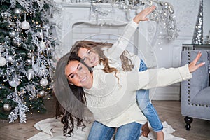 Happy family on New Year Eve. Young beautiful mother and little cute daughter in white cozy sweaters and blanket have fun and hug