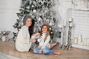 Happy family on New Year Eve. Young beautiful mother and little cute daughter in white cozy sweaters and blanket have fun and hug