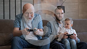 Happy family old grandpa's son and grandson are playing video game on console, holding joystick and pressing sit buttons