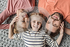 Happy family with one child lying together on grey knitted carpet