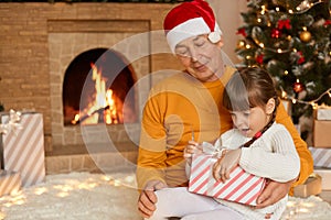 Happy family opening christmas presents, cute astonished child unpacking ribbon with big eyes and opened mouth, sit on grandad`s