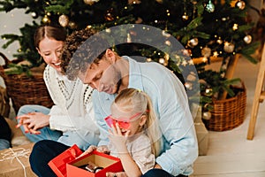 Happy family opening gifts while sitting on floor near Christmas tree