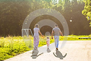 Happy family outdoor activity. Rear view of parents and baby daughter having fun and walking in summer park.