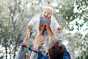 Happy family outdoors activity, father raises baby up, laughing and playing, father shows mother how to throws baby with safety