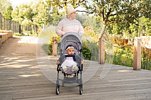 Happy family outdoors, a mother walks with a little toddler in a stroller in the summer on nature