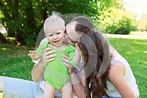 Happy family outdoors mum and dad hold and kiss baby