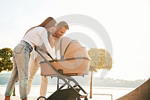 Happy family outdoors. A young couple with a baby pram is walking together