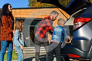 Happy family packing luggage to the trunk of a car before moving to a new home or going to vacations.