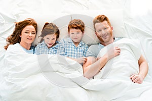 happy family in pajamas lying in bed and smiling