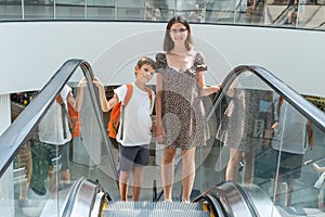 A happy family with paper bags is standing on an escalator in a shopping mall and discussing their purchases