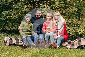 happy family with paper cups smiling at camera while sitting together