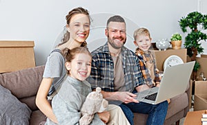 Happy family parents and children move to new apartment and sit on  couch among the boxes studying information on the Internet