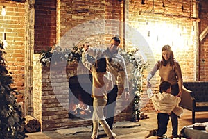 Happy family parents with two kids dancing together near fireplace