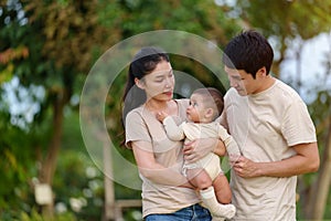 happy family in park. father and mother talking and playing with infant baby