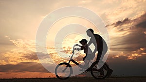 happy family in the park. father teaching son to ride a bike at sunset silhouette in the park. son child learning to