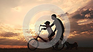 happy family in the park. father teaching son to ride a bike at sunset silhouette in the park. son child learning to