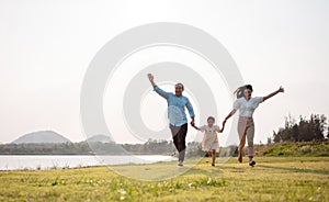 Happy family in the park sunset light. family on weekend running together in the meadow with river Parents hold the child hands.